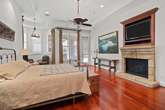 bedroom with visible vents, a raised ceiling, a stone fireplace, dark wood-style floors, and recessed lighting
