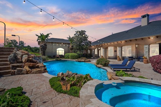 pool at dusk with a patio area, an in ground hot tub, and an outdoor pool