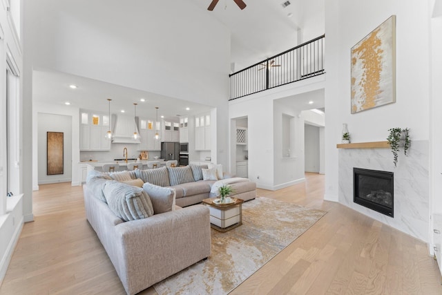 living room featuring baseboards, a high ceiling, a ceiling fan, light wood-style flooring, and a premium fireplace