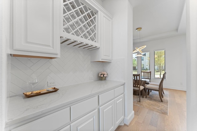 bar featuring an inviting chandelier, tasteful backsplash, hanging light fixtures, light wood finished floors, and baseboards