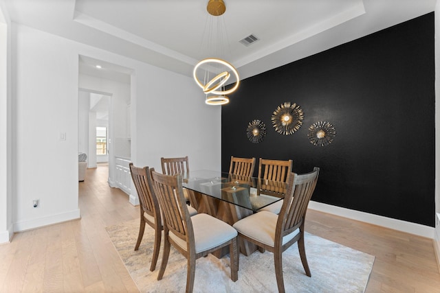 dining space featuring a tray ceiling, visible vents, and light wood-style flooring