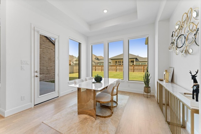 dining area with baseboards, light wood-type flooring, and a raised ceiling