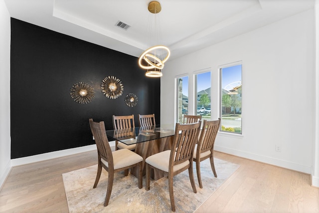 dining area with visible vents, baseboards, a tray ceiling, and wood finished floors