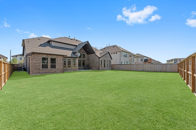 back of house with roof with shingles, a yard, a fenced backyard, and brick siding