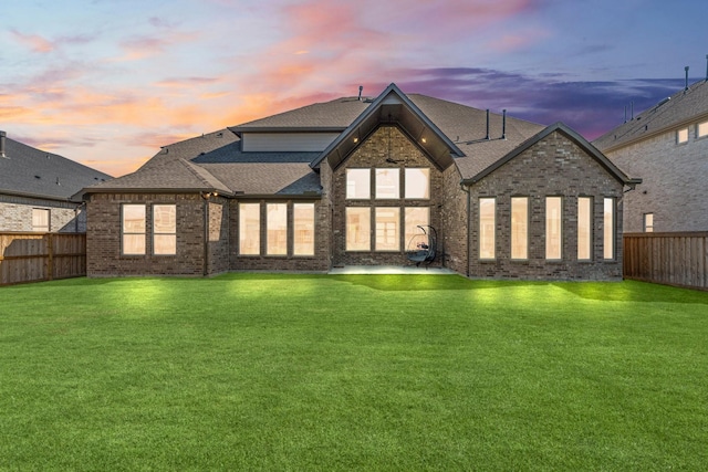 rear view of property featuring a yard, brick siding, and a fenced backyard