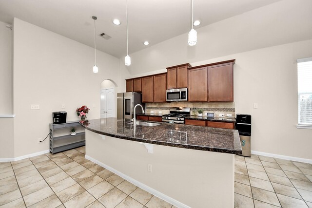kitchen featuring light tile patterned floors, tasteful backsplash, a sink, appliances with stainless steel finishes, and an island with sink