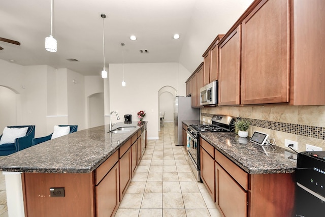 kitchen with tasteful backsplash, arched walkways, stainless steel appliances, brown cabinets, and a sink