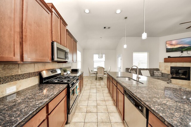 kitchen with a sink, visible vents, stainless steel appliances, a tiled fireplace, and brown cabinetry
