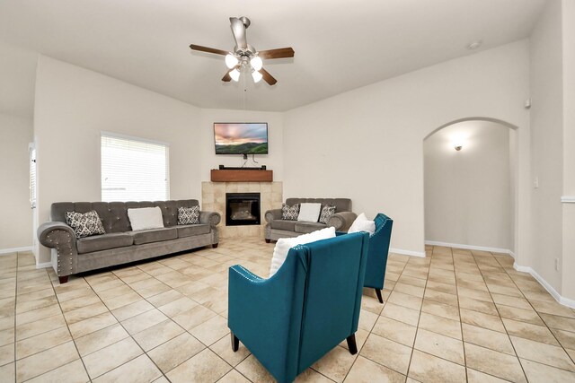 living room with arched walkways, a tile fireplace, light tile patterned floors, baseboards, and a ceiling fan