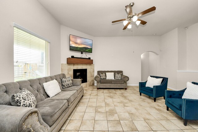 living room featuring light tile patterned floors, a tiled fireplace, a ceiling fan, and arched walkways