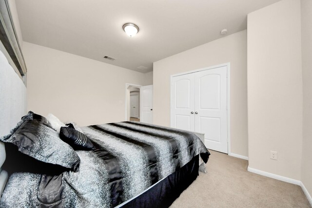 bedroom with a closet, visible vents, light colored carpet, and baseboards