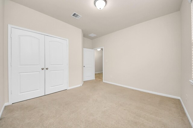 unfurnished bedroom featuring light colored carpet, visible vents, a closet, and baseboards