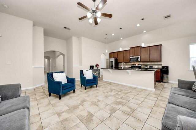 living room with arched walkways, light tile patterned floors, ceiling fan, visible vents, and high vaulted ceiling