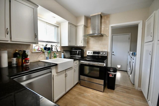 kitchen with washer and dryer, wall chimney exhaust hood, a sink, appliances with stainless steel finishes, and dark countertops
