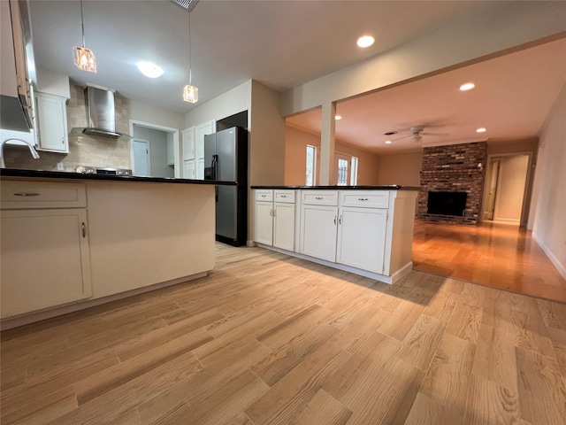 kitchen featuring stainless steel fridge, wall chimney exhaust hood, dark countertops, light wood-style floors, and a peninsula