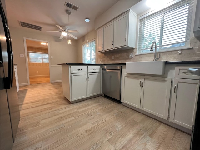 kitchen with light wood finished floors, a peninsula, stainless steel dishwasher, and visible vents