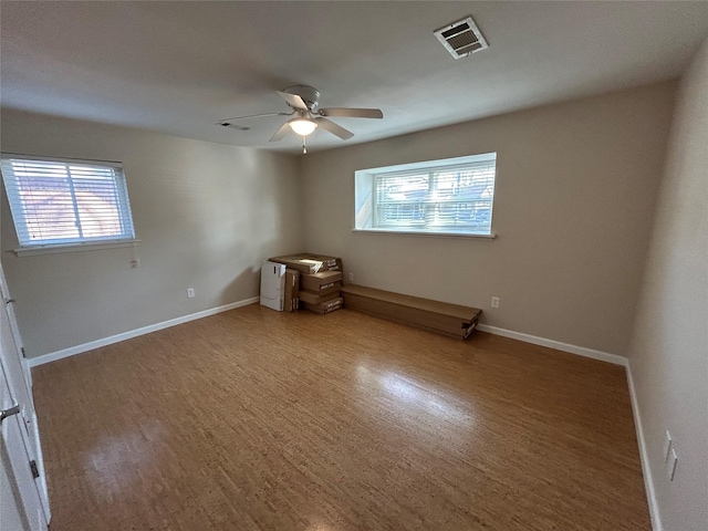 spare room with wood finished floors, ceiling fan, visible vents, and plenty of natural light