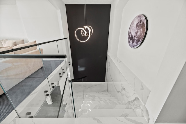 stairway with marble finish floor and an inviting chandelier