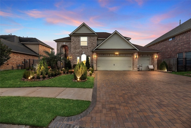 traditional-style home featuring decorative driveway, brick siding, a garage, fence, and a lawn