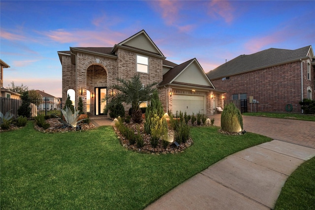 traditional-style house featuring decorative driveway, fence, a front lawn, brick siding, and an attached garage