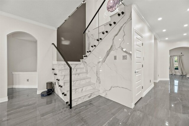 stairway featuring arched walkways, marble finish floor, crown molding, and baseboards