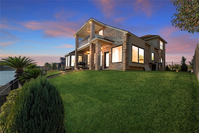 property exterior at dusk with a yard, brick siding, a balcony, and a fenced backyard