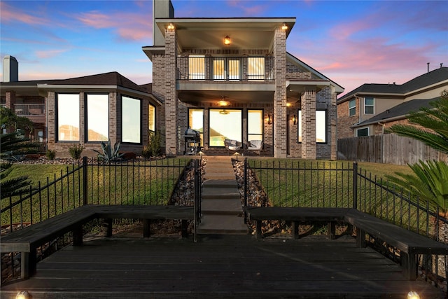 back of house at dusk with a yard, brick siding, a balcony, and fence private yard