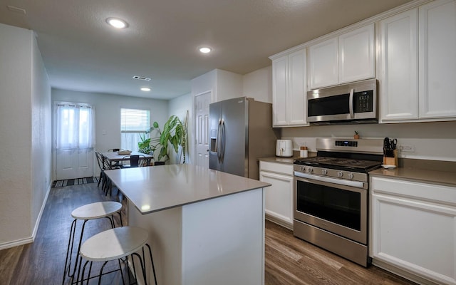 kitchen with visible vents, white cabinets, appliances with stainless steel finishes, a kitchen bar, and dark wood finished floors