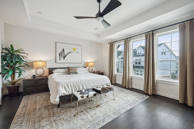 bedroom with a raised ceiling, visible vents, dark wood-style flooring, baseboards, and ceiling fan