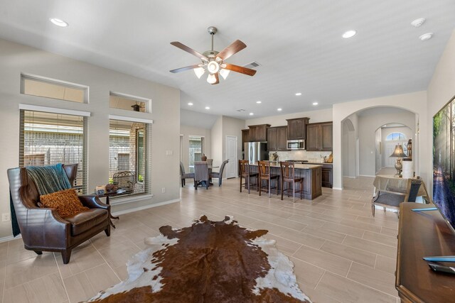 living room with baseboards, a ceiling fan, arched walkways, and a healthy amount of sunlight