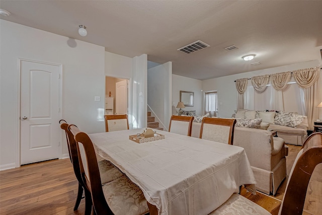dining space featuring stairs, light wood finished floors, visible vents, and baseboards