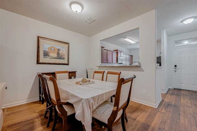 dining space with visible vents, baseboards, hardwood / wood-style floors, and a textured ceiling