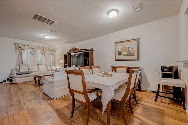 dining area featuring visible vents, light wood finished floors, and a textured ceiling