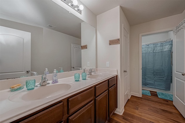 bathroom featuring a sink, visible vents, double vanity, and wood finished floors