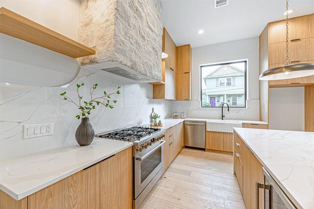 kitchen featuring stainless steel appliances, light stone countertops, modern cabinets, and a sink