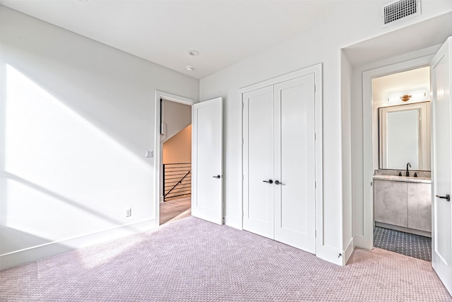 unfurnished bedroom featuring visible vents, a closet, a sink, carpet, and ensuite bath