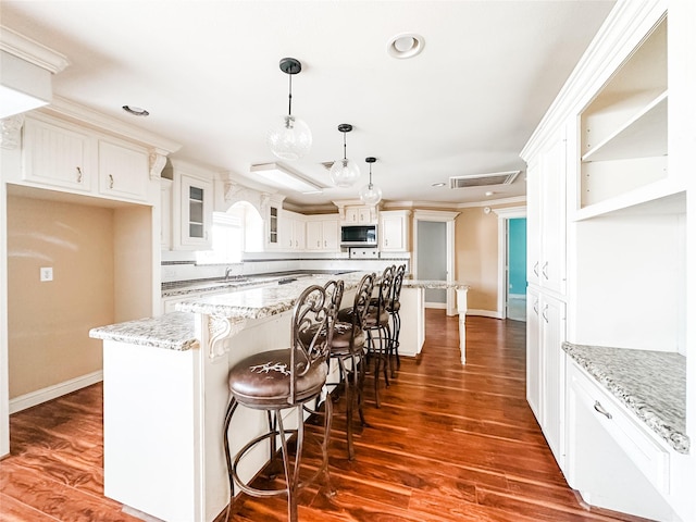 kitchen with glass insert cabinets, visible vents, a center island, stainless steel microwave, and baseboards
