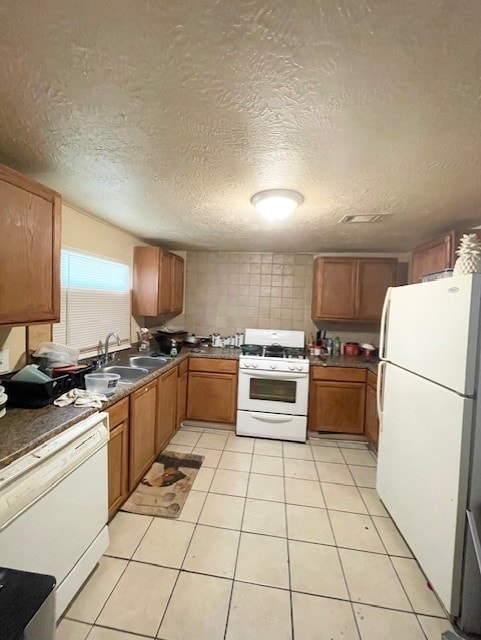 kitchen with white appliances, brown cabinetry, a textured ceiling, light tile patterned flooring, and a sink