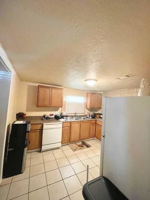 kitchen with a textured ceiling, brown cabinets, light tile patterned floors, and white appliances