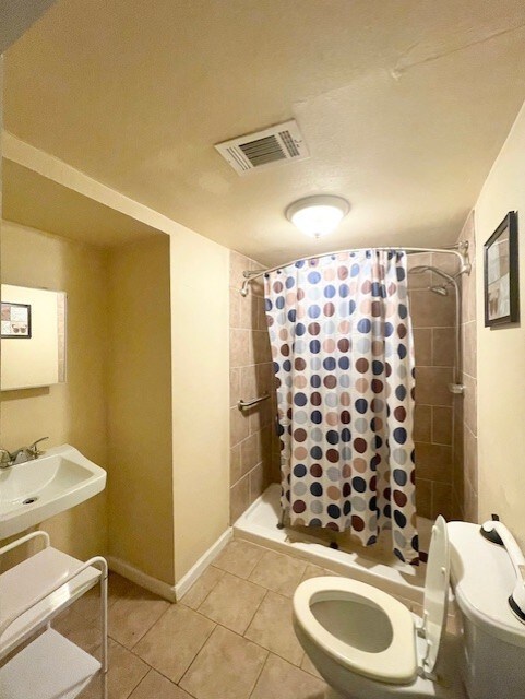 full bathroom with a tile shower, tile patterned flooring, visible vents, toilet, and a sink