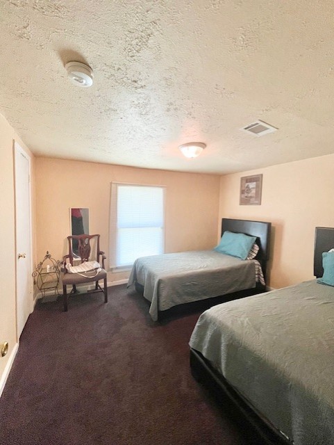 bedroom with a textured ceiling, dark colored carpet, and visible vents