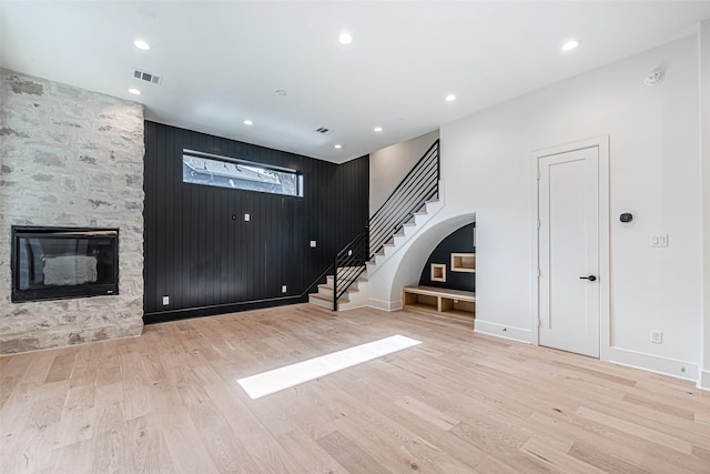unfurnished living room with a fireplace, visible vents, stairs, and wood finished floors