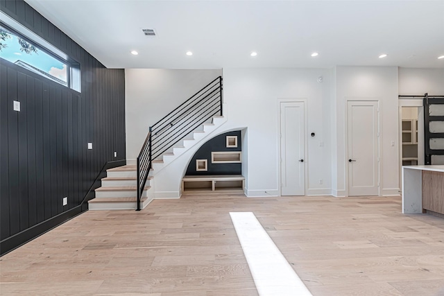 foyer featuring visible vents, a barn door, light wood-style floors, and stairs