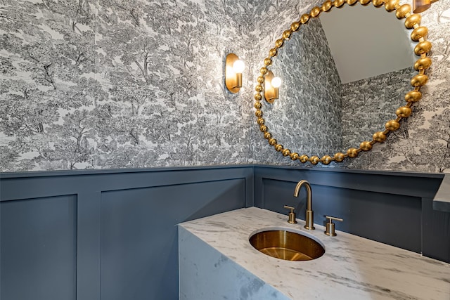 bathroom featuring a decorative wall, vanity, and wainscoting