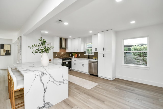kitchen featuring wall chimney range hood, visible vents, light stone counters, dishwasher, and gas range oven