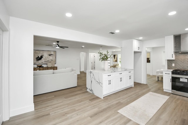 kitchen featuring open floor plan, range with gas stovetop, white cabinetry, and backsplash