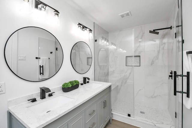 full bath with a sink, visible vents, a marble finish shower, and double vanity