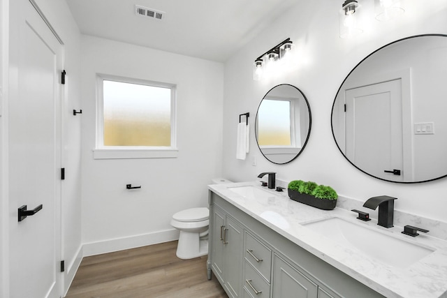 bathroom with visible vents, baseboards, a sink, toilet, and double vanity