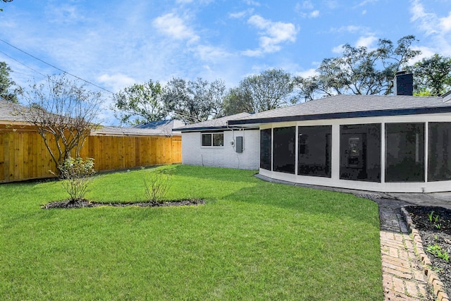 back of property with a sunroom, a fenced backyard, a chimney, and a lawn