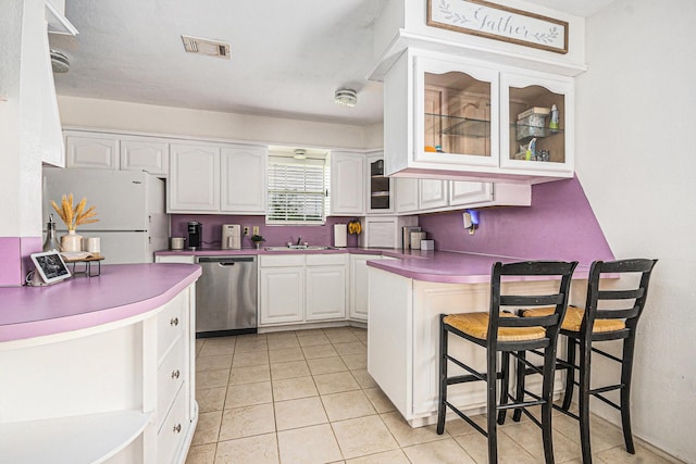 kitchen featuring a kitchen breakfast bar, dishwasher, a peninsula, visible vents, and freestanding refrigerator